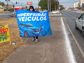 Agente segurando bandeira horizontal próximo a via urbana, como referência de posicionamento